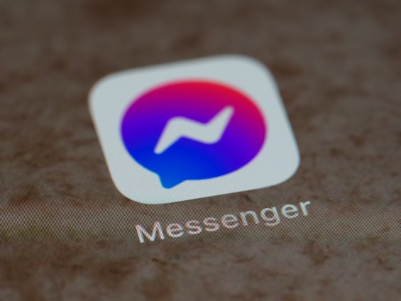 A close-up view of a smartphone screen displaying the Messenger app icon, which is a speech bubble with a gradient from blue to pink and a white lightning bolt in the center.
