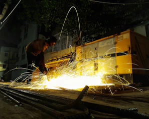 Bright welding arc illuminating a nighttime roadside repair on a heavy machinery part