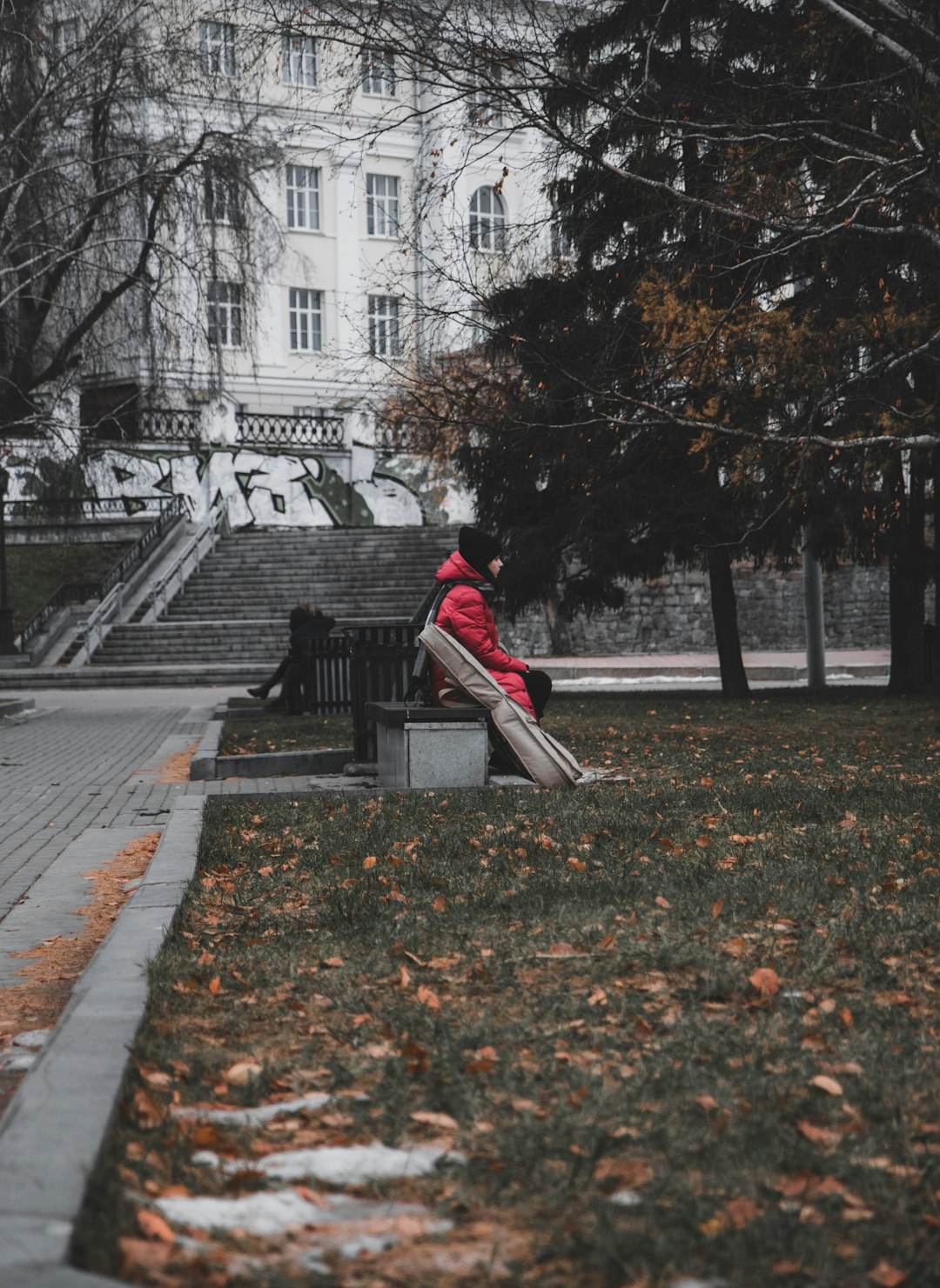 woman in red jacket and gray pants sitting on gray concrete stairs
