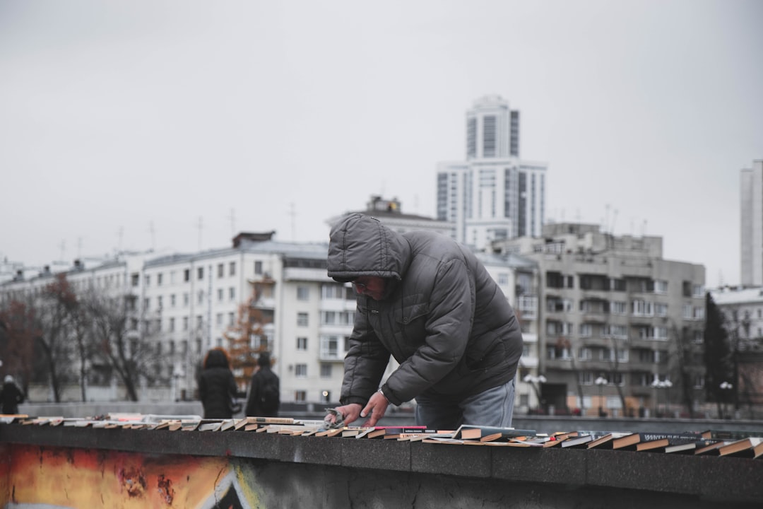 man in black jacket and gray pants sitting on concrete wall during daytime