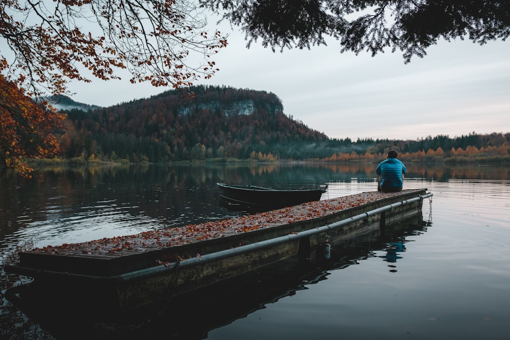 man in blue jacket sitting on brown wooden dock during daytime