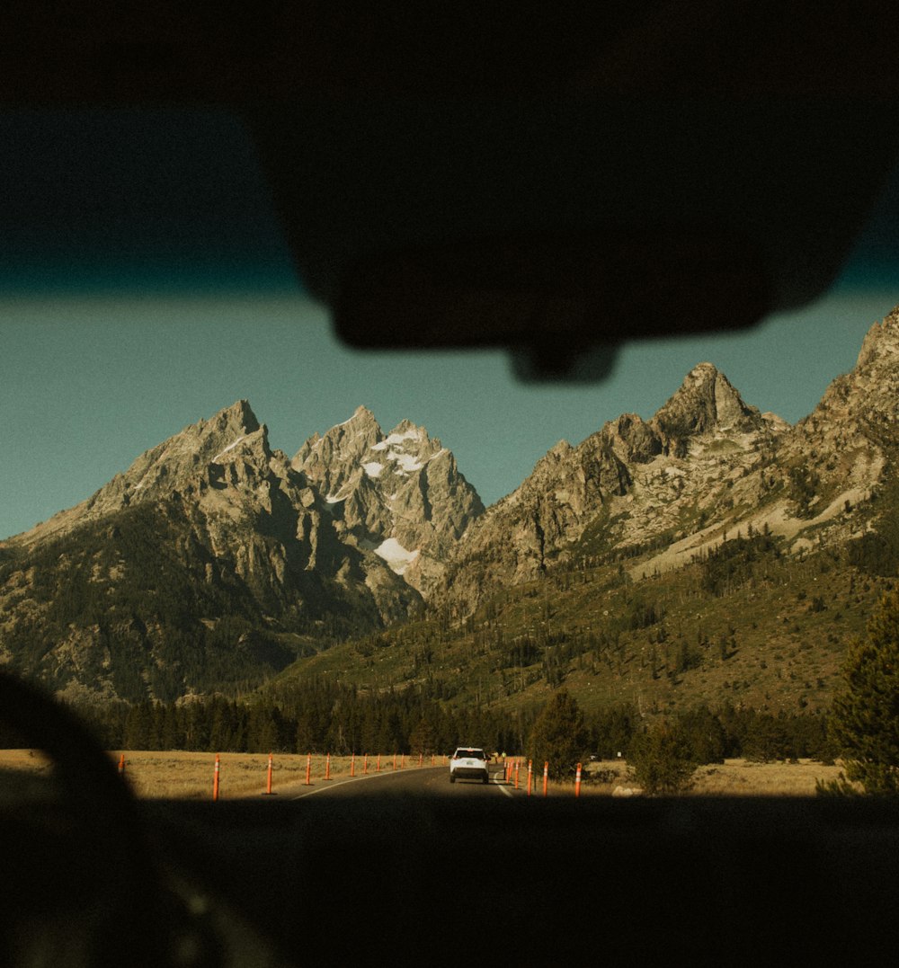 white car on road near green grass field and mountain during daytime