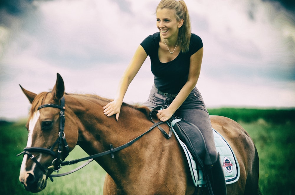 Mujer con camiseta azul de cuello redondo montando caballo marrón durante el día
