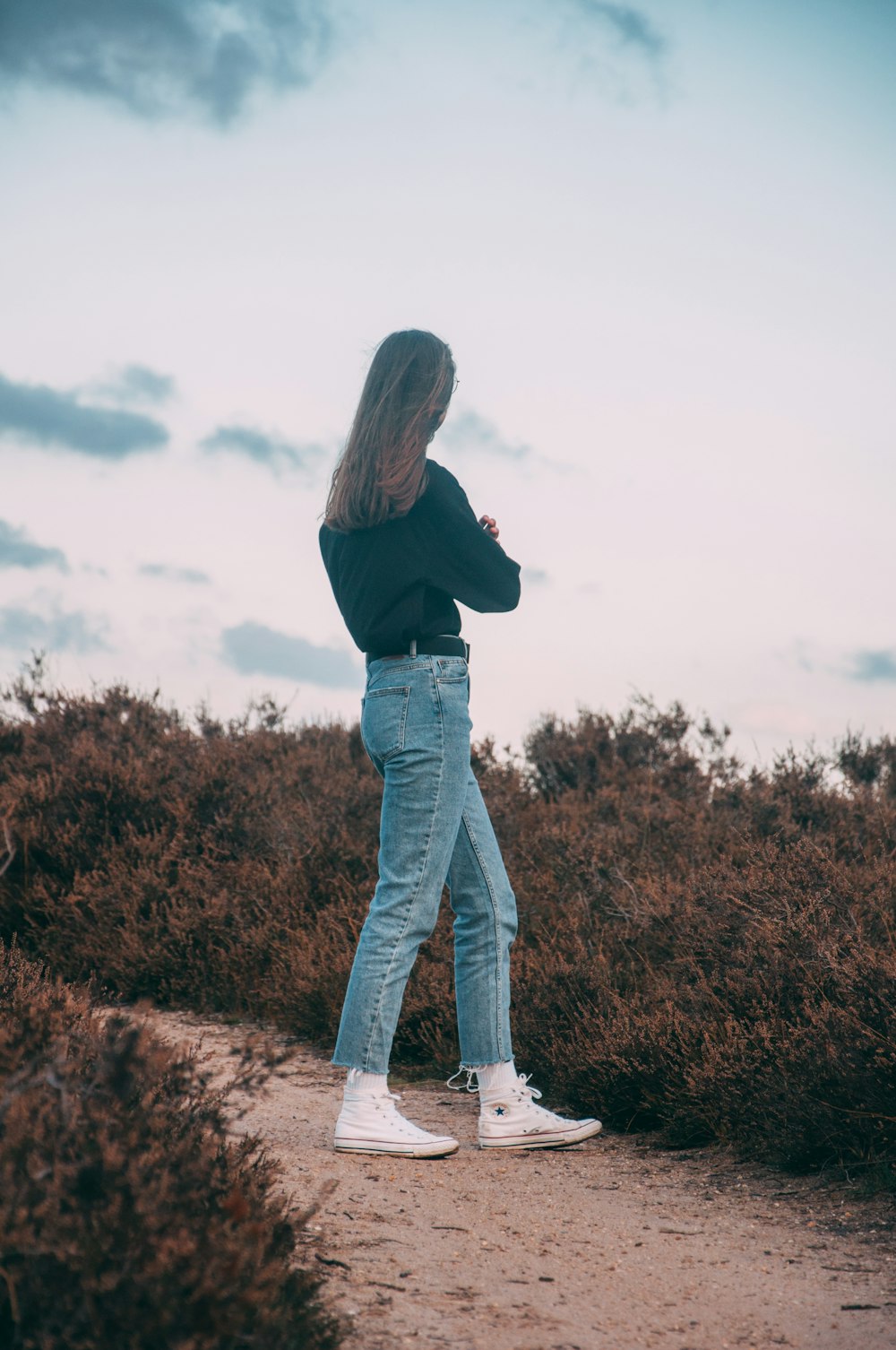 woman in black long sleeve shirt and blue denim jeans standing on brown grass field during