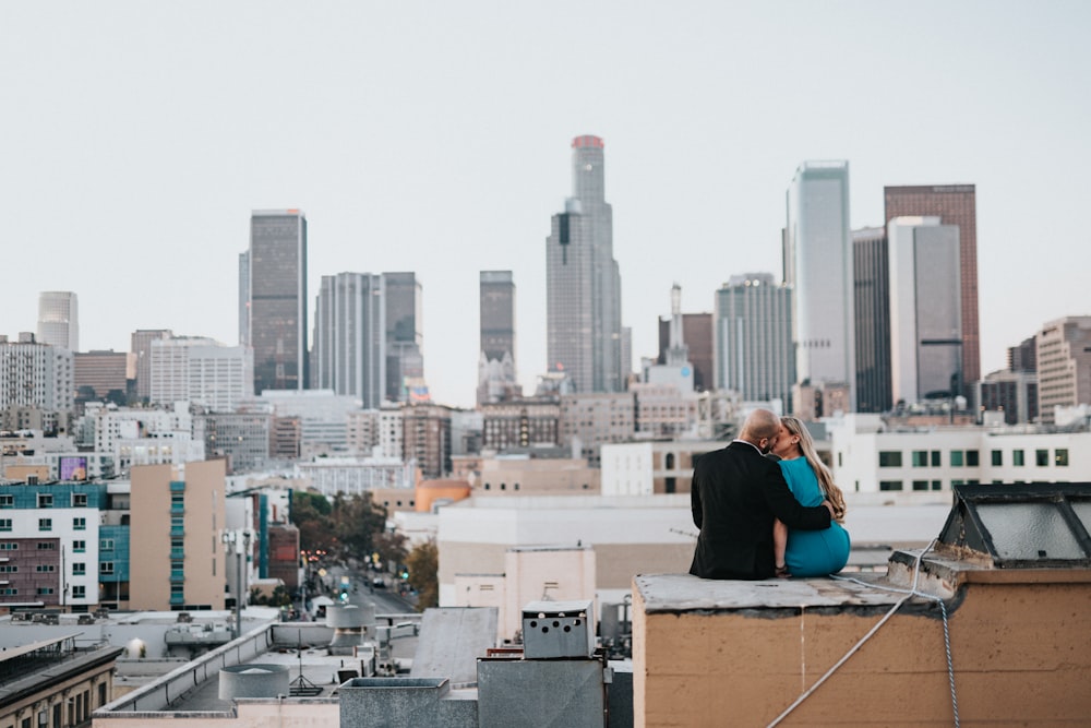 man in blue long sleeve shirt sitting on brown wooden table looking at city buildings during