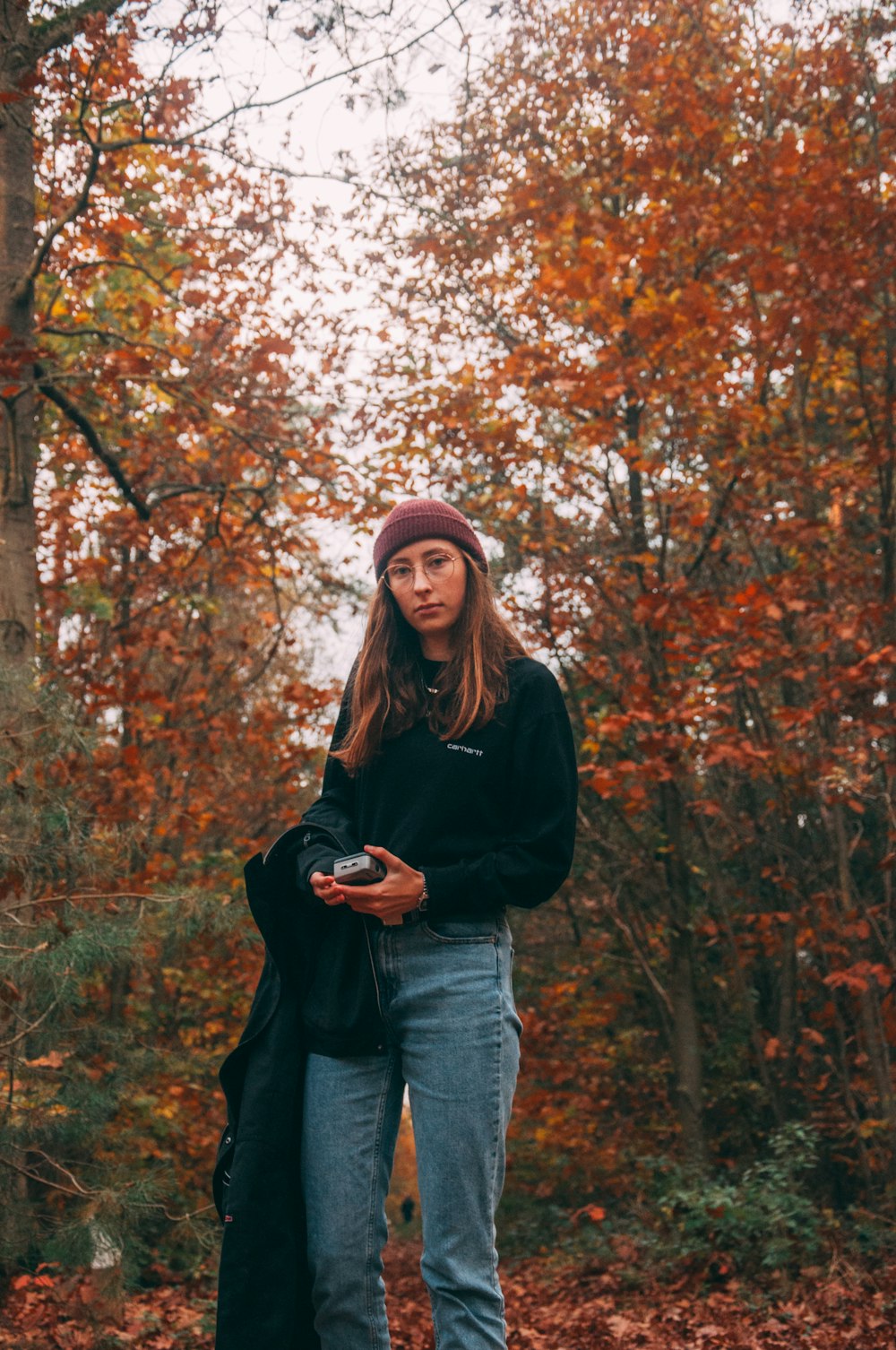 woman in black long sleeve shirt and blue denim jeans standing near brown trees during daytime