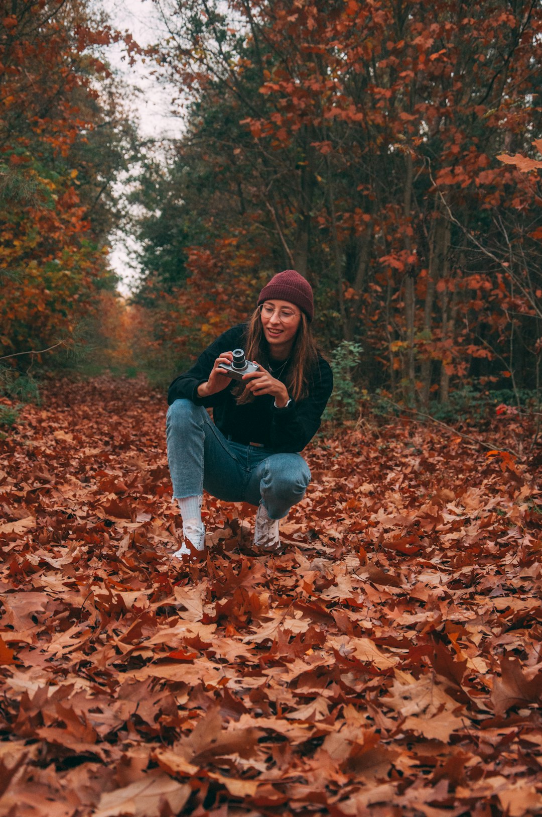 woman in black hoodie and blue denim jeans sitting on brown dried leaves during daytime