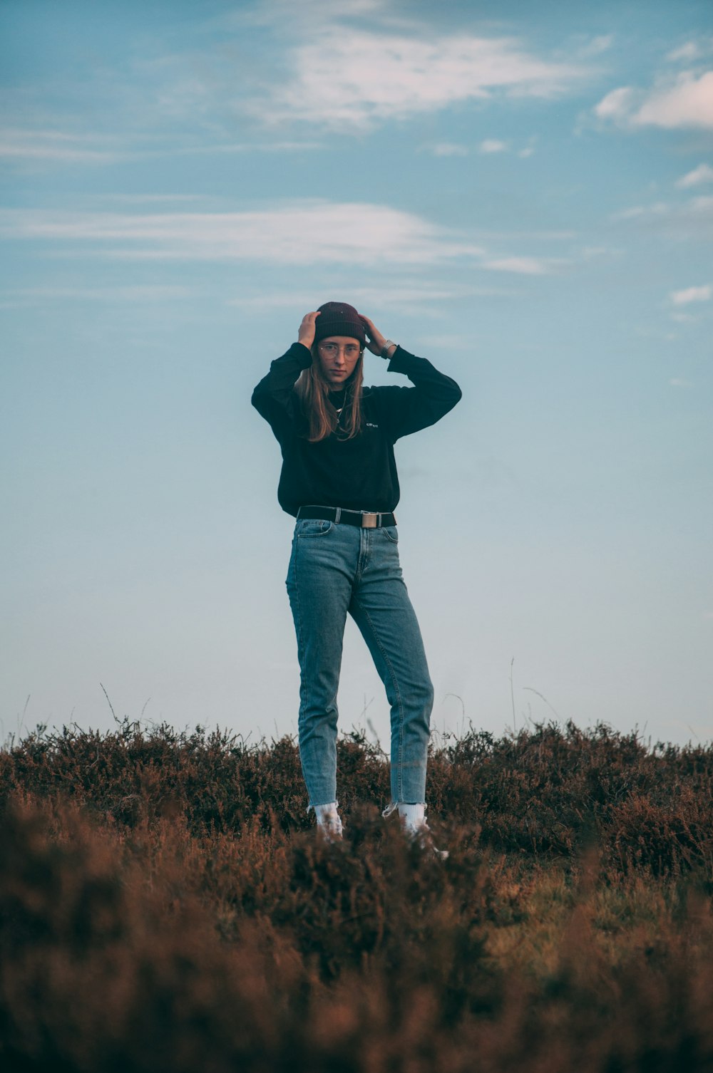 woman in black jacket and blue denim jeans standing on brown grass field