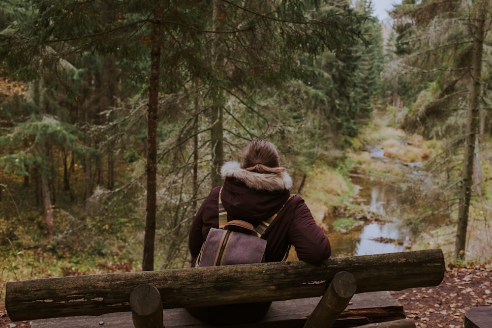 woman in brown jacket sitting on brown wooden bench near lake during daytime