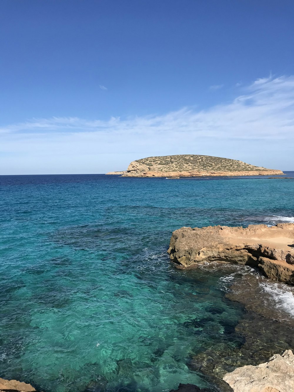 Formación rocosa marrón en el mar azul bajo el cielo azul durante el día