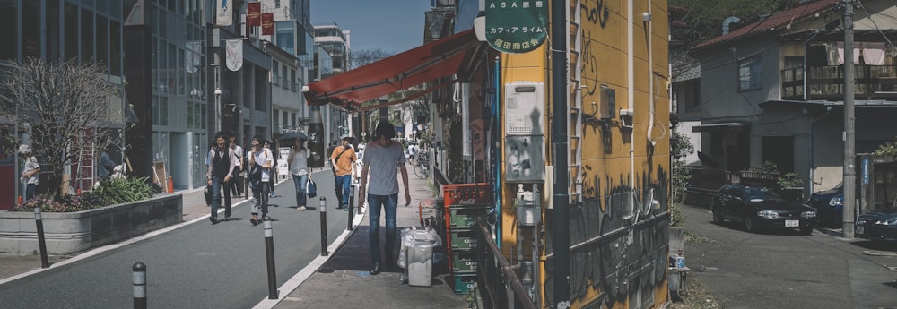 homem em camisa social azul e jeans jeans azul em pé ao lado da loja amarela e verde durante