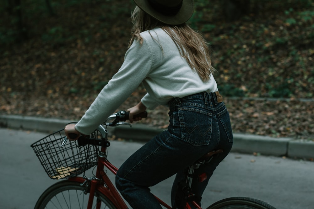 woman in white long sleeve shirt and blue denim jeans riding red bicycle during daytime