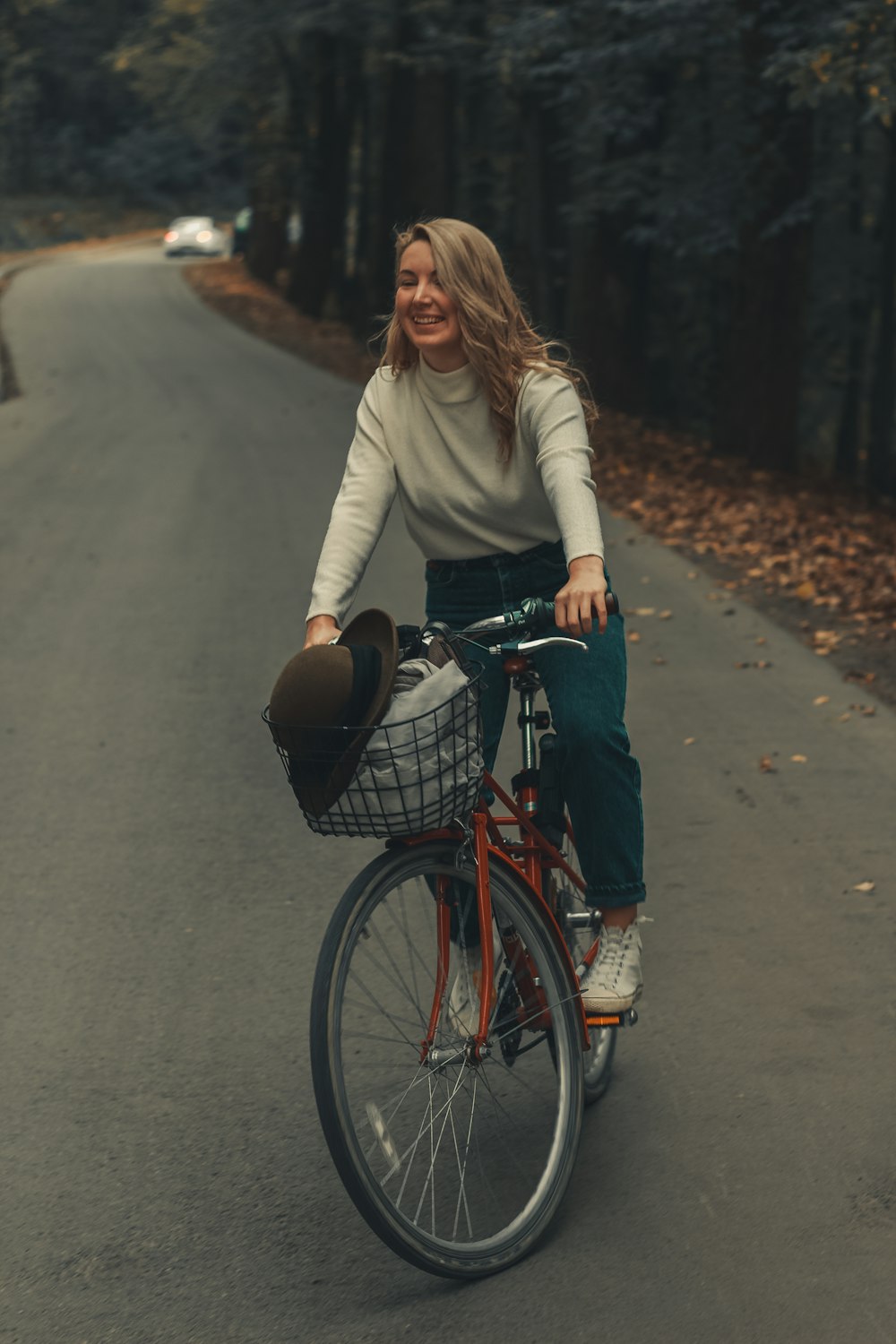 woman in beige sweater and blue denim jeans riding on black bicycle on gray concrete road
