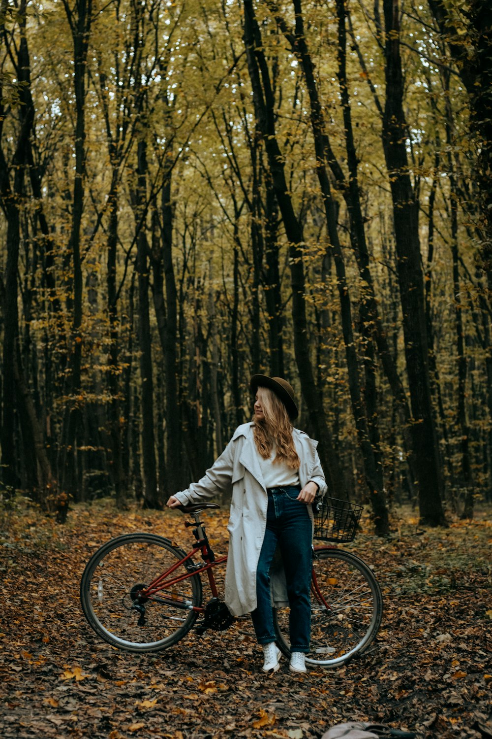 woman in white long sleeve shirt and blue denim jeans standing on forest with bicycle