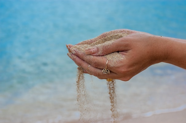 A close-up of intertwined hands resting gently on a sandy beach