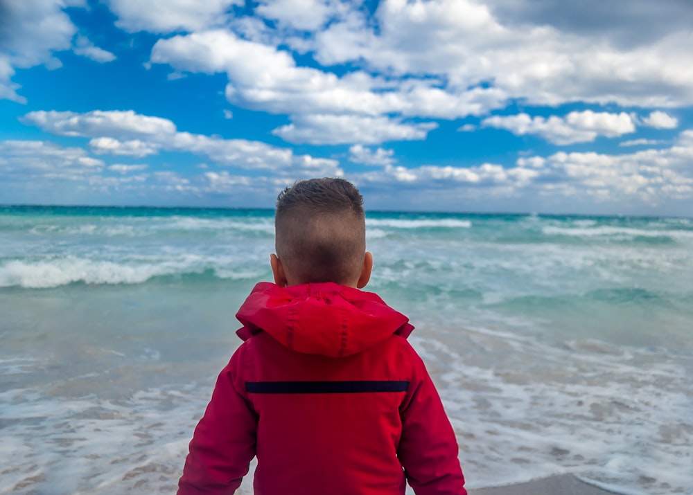 boy in red hoodie standing on beach during daytime