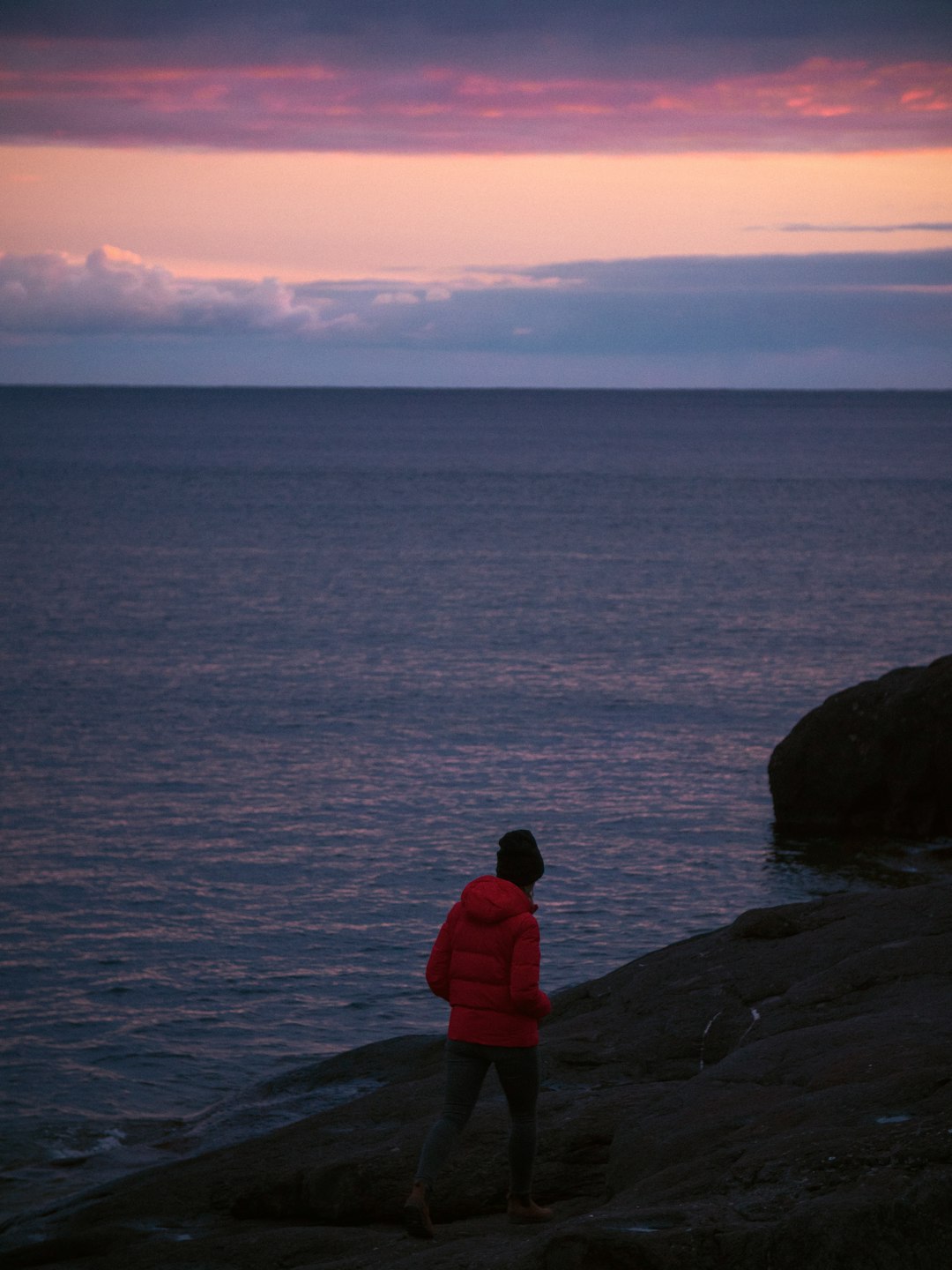 man in red hoodie sitting on rock near body of water during daytime