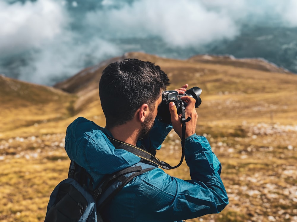 hombre en chaqueta azul tomando foto de la montaña