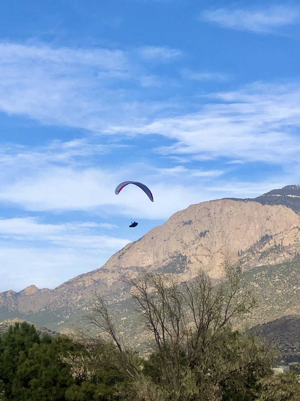 person riding parachute over brown rocky mountain during daytime