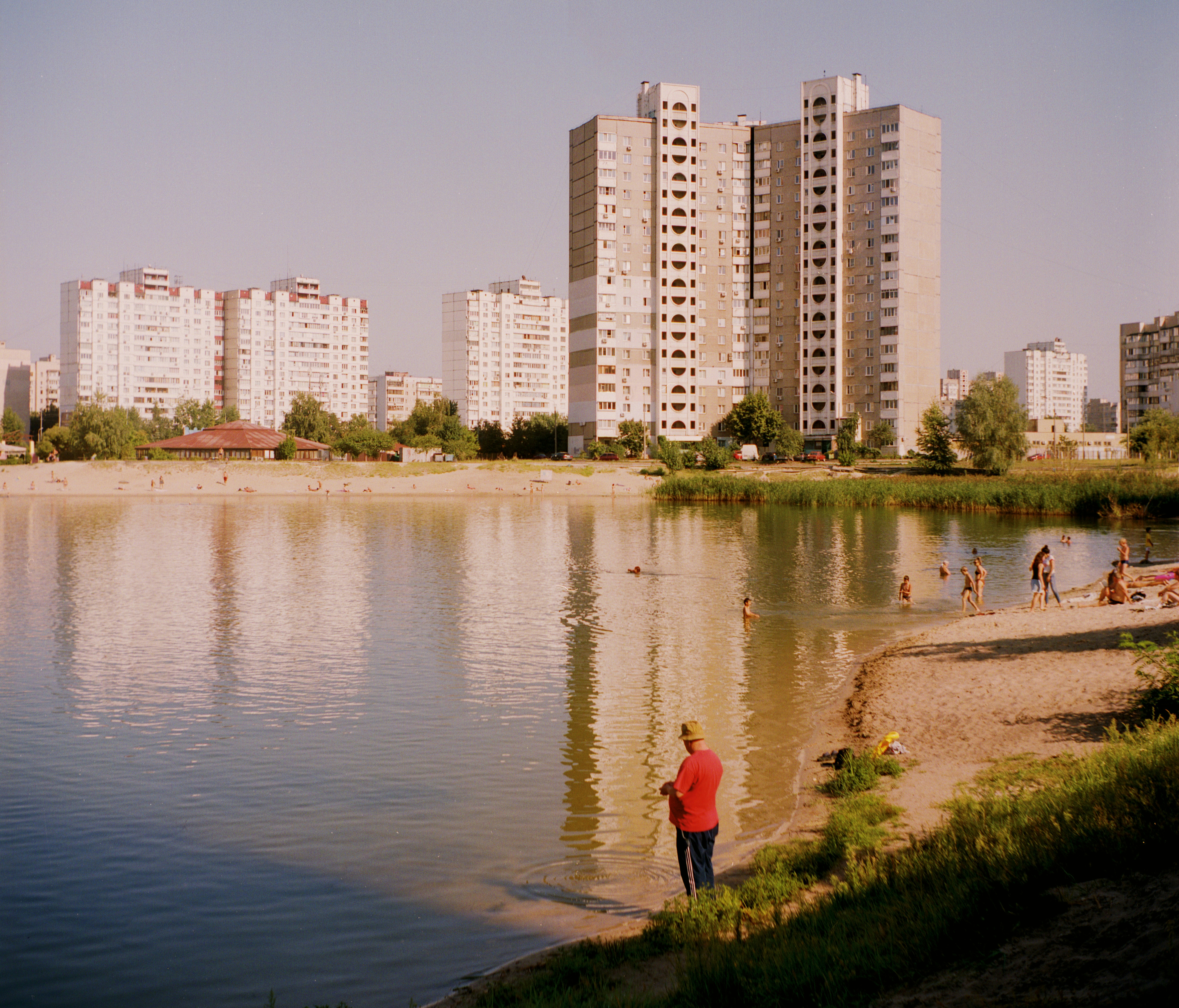 woman in red jacket walking on green grass near body of water during daytime