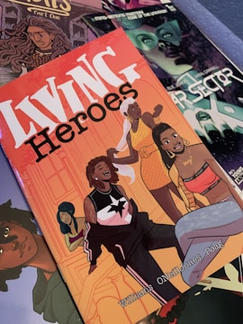 A collection of comic book covers is displayed, featuring vibrant illustrations. The prominent cover, 'Living Heroes,' showcases several animated characters, each with distinct styles and expressions, possibly indicating a diverse group of superheroes. The background includes other comic covers with detailed artwork in various colors.