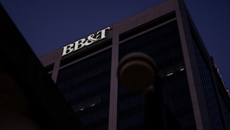 A tall office building under a dark sky, prominently featuring the letters 'BB&T' at the top. The structure is designed with large glass windows and concrete frameworks, creating a modern architectural appearance.