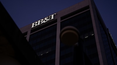 A tall office building under a dark sky, prominently featuring the letters 'BB&T' at the top. The structure is designed with large glass windows and concrete frameworks, creating a modern architectural appearance.
