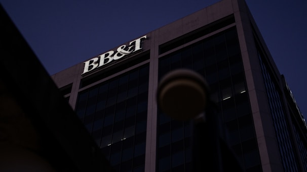 A tall office building under a dark sky, prominently featuring the letters 'BB&T' at the top. The structure is designed with large glass windows and concrete frameworks, creating a modern architectural appearance.