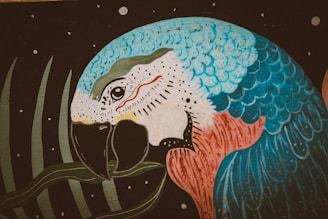 A vibrantly colored painting of a parrot with predominantly blue, white, and red feathers against a dark backdrop with a few scattered small white circles. The parrot is holding a green leaf in its beak.