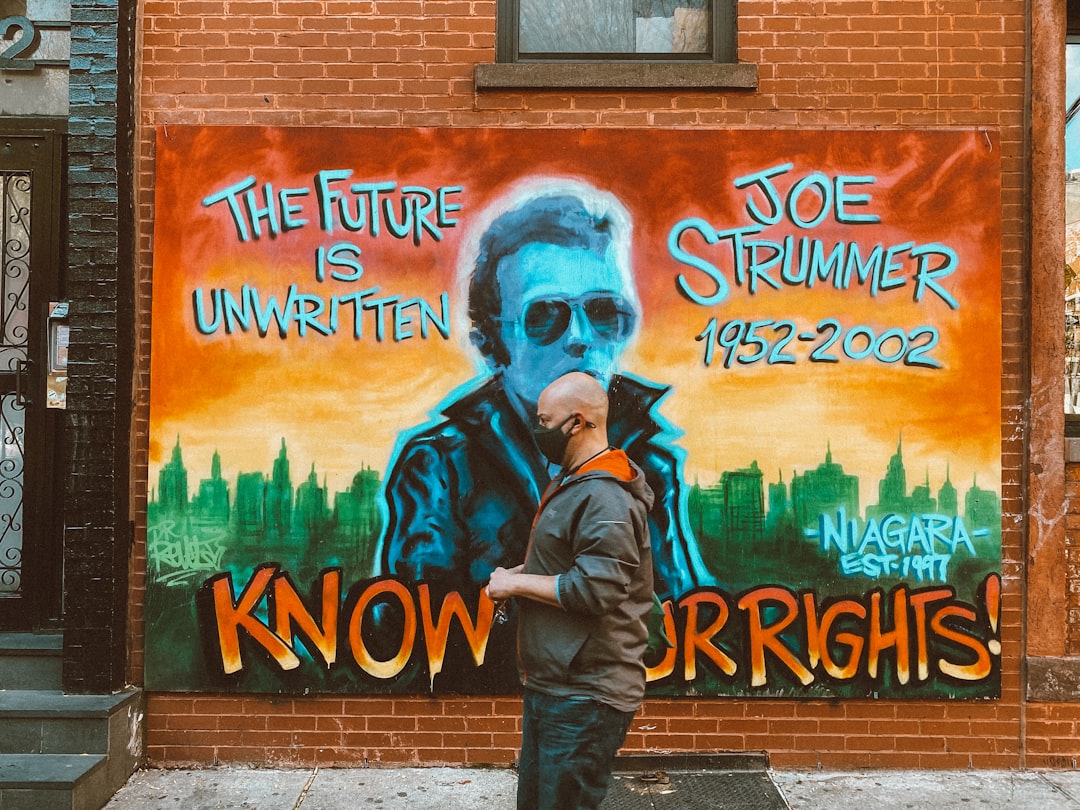 man in black jacket and blue denim jeans standing beside wall with graffiti