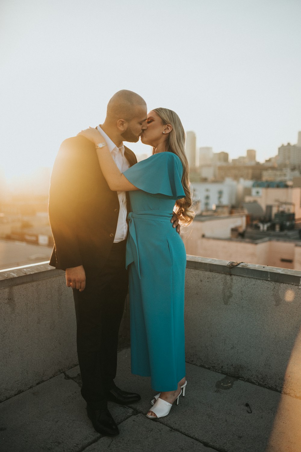 Mujer en vestido azul sin mangas de pie junto a hombre en traje negro