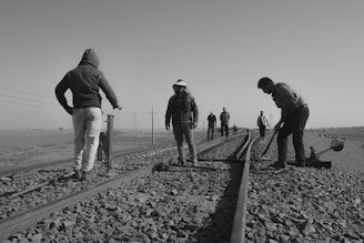 grayscale photo of people walking on train rail