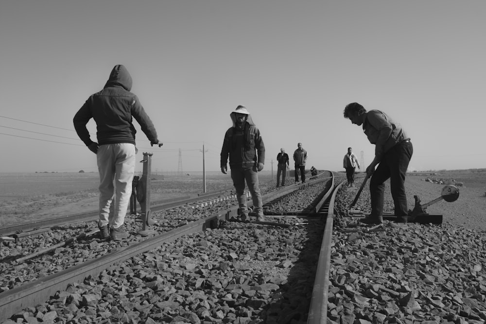 Foto en escala de grises de personas caminando sobre el riel del tren
