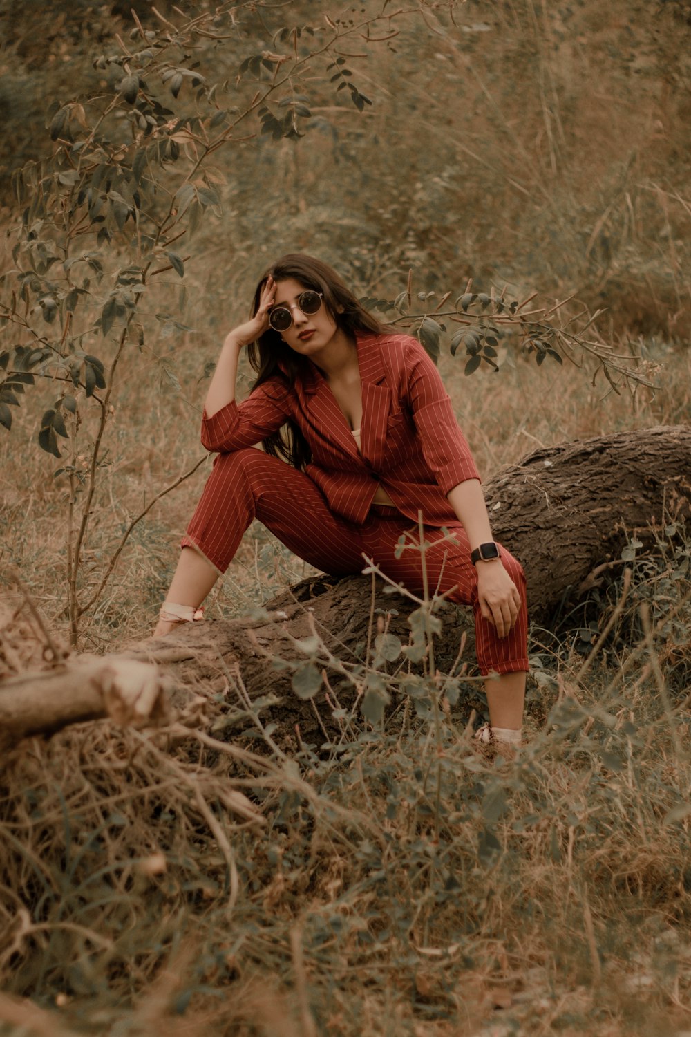 donna in camicia rossa a maniche lunghe e pantaloni marroni seduta su erba marrone durante il giorno