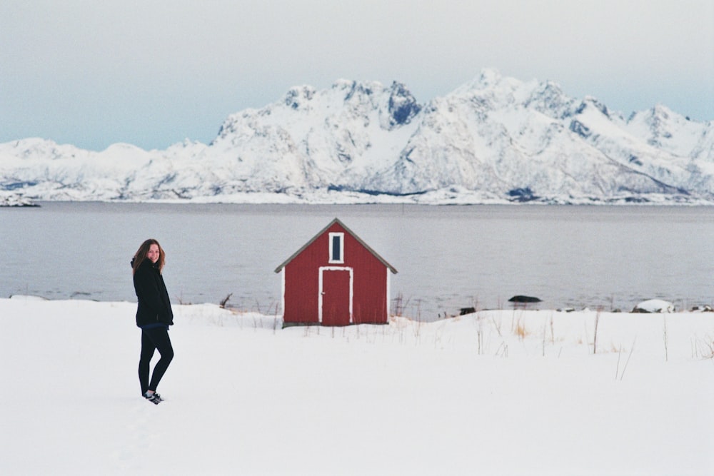 man in black jacket and black pants standing on snow covered ground near red house during