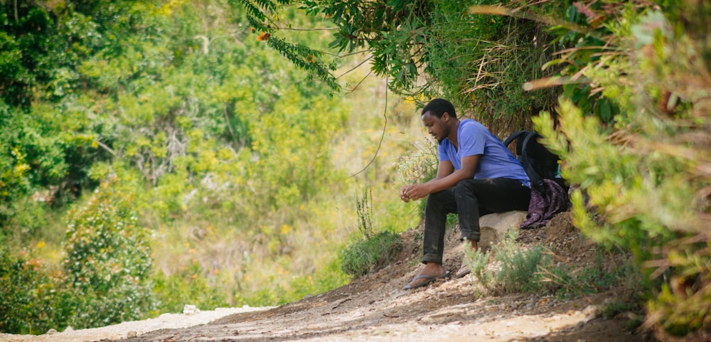파란색 티셔츠와 검은 바지를 입은 남자가 낮에 갈색 나무 줄기에 앉아 있다