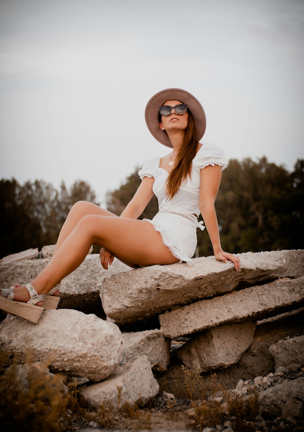 woman in white tank top and white shorts sitting on brown rock during daytime