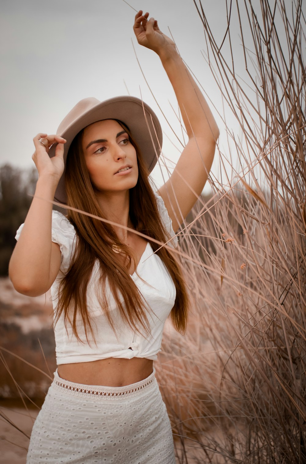 woman in white crop top and brown hat standing on brown field during daytime