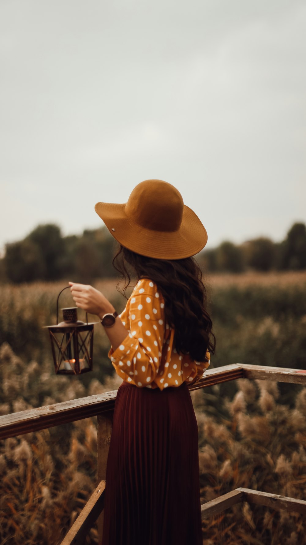 woman in brown sun hat and black and white polka dot dress holding brown wooden fence
