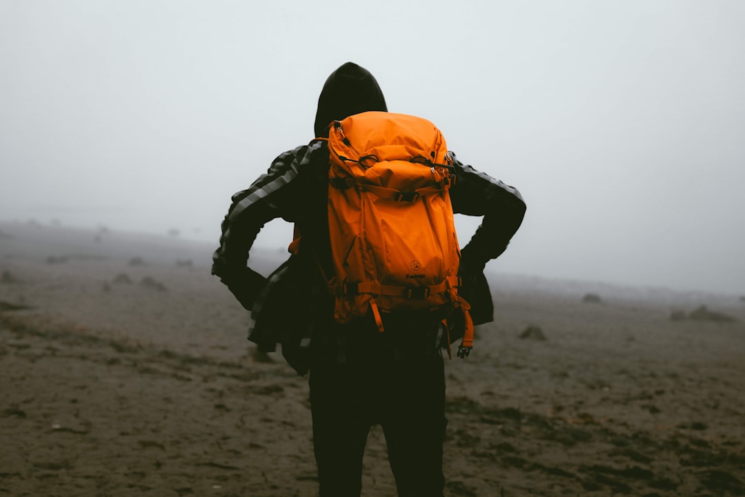 man in orange and black jacket and black pants standing on brown sand during daytime