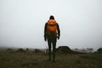 man in orange jacket and black pants standing on brown field during daytime