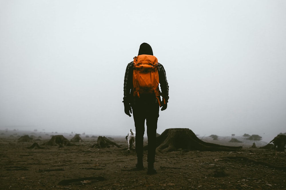 man in orange jacket and black pants standing on brown field during daytime