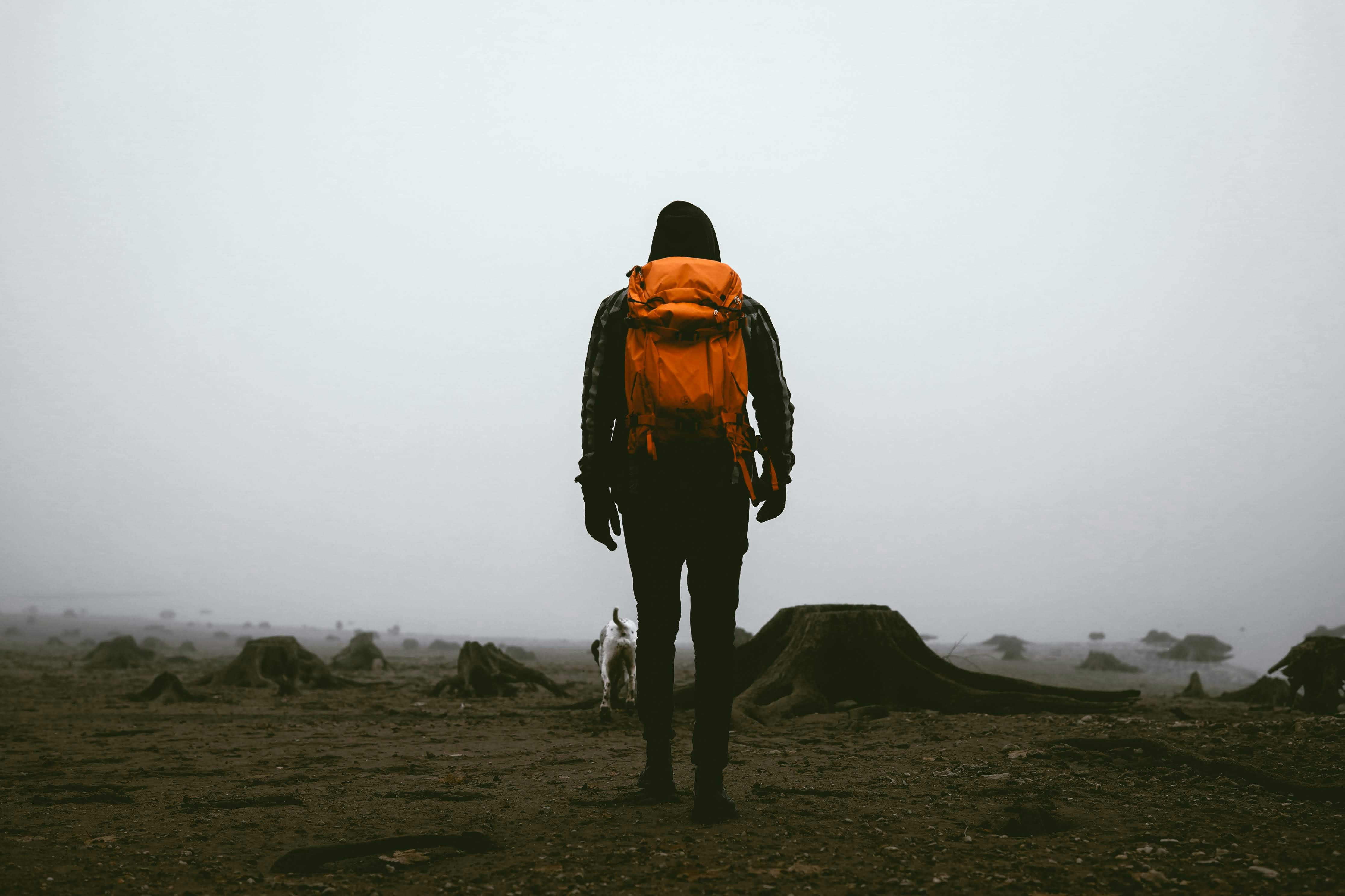 man in orange jacket and black pants standing on brown field during daytime