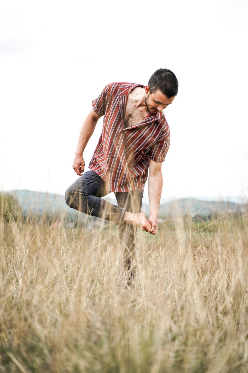 man in brown and white stripe polo shirt and blue denim jeans sitting on brown grass