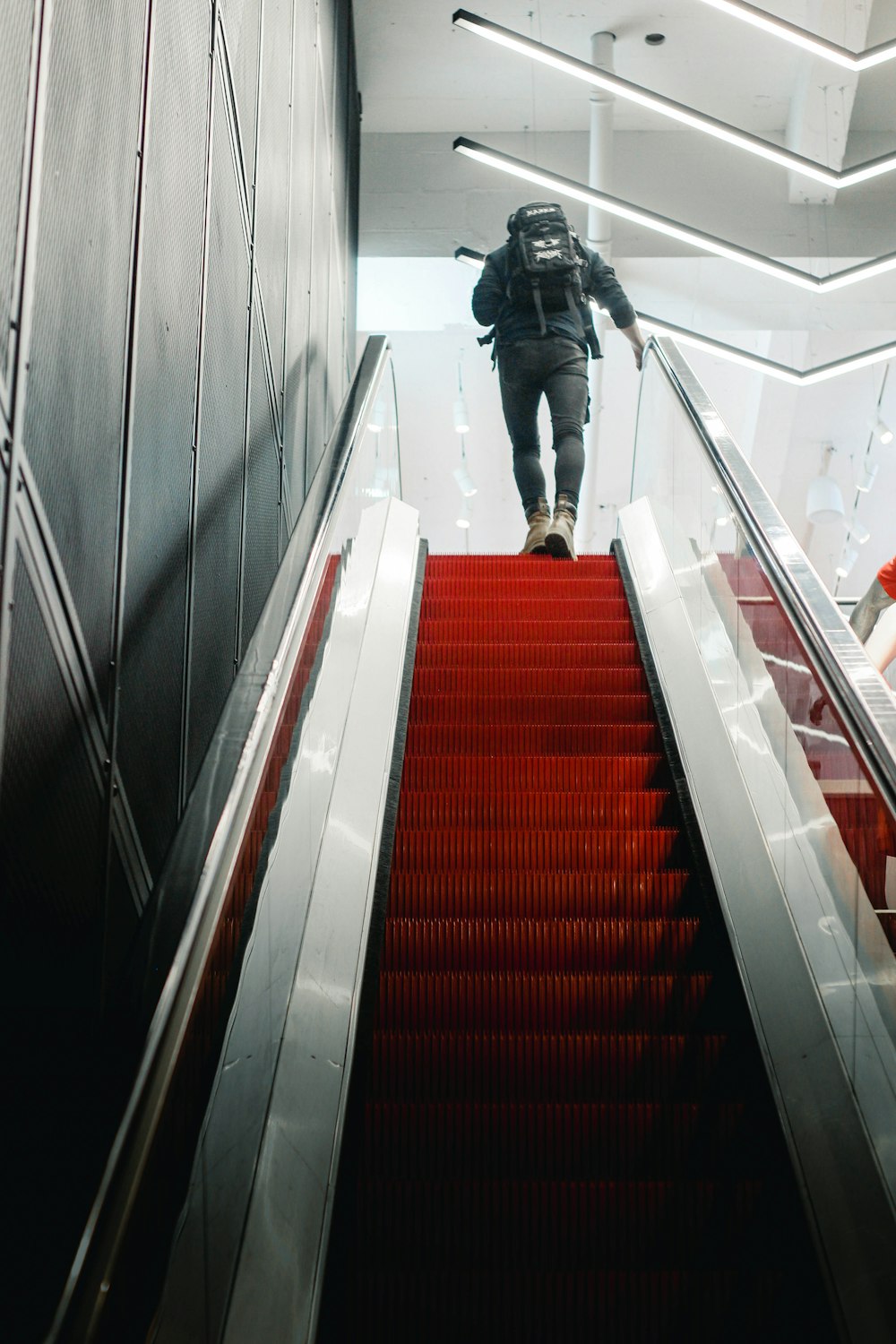 man in black jacket and blue denim jeans walking on red and white staircase