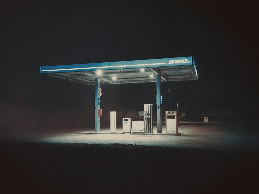 Une station-service éclairée la nuit, son auvent bleu au-dessus de quelques pompes, dans l’obscurité