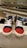A display features a pair of children's sneakers with navy blue fabric and bright red toes, white laces, and white soles. They are placed on a shelf in a shoe store with other footwear visible in the background, arranged neatly on several shelves.
