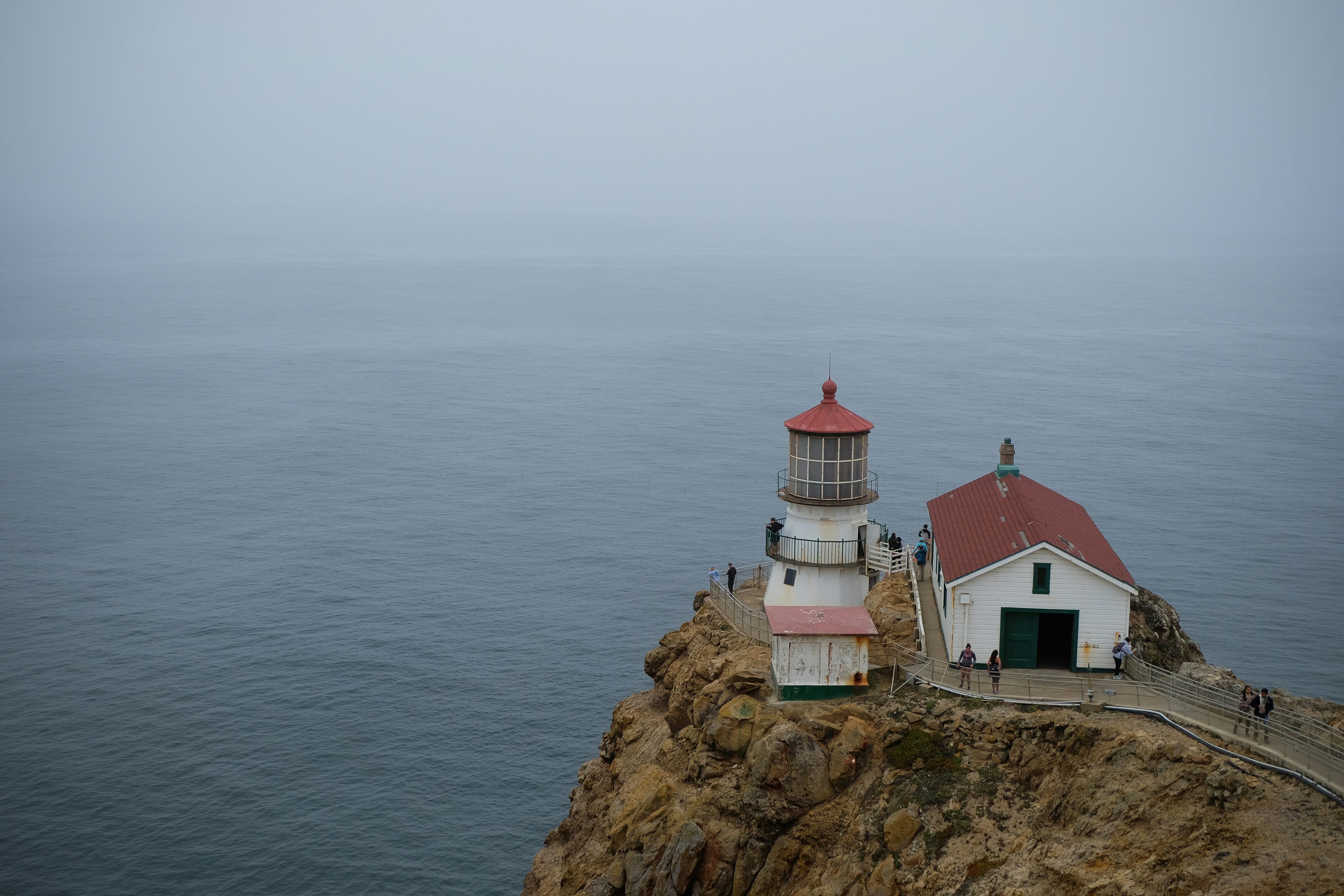 white and red concrete house on brown rock formation near body of water during daytime, Point Reyes Lighthouse