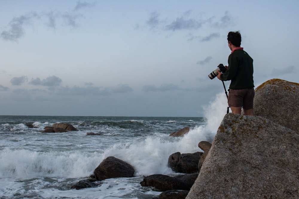 man in black jacket and black pants standing on rocky shore during daytime