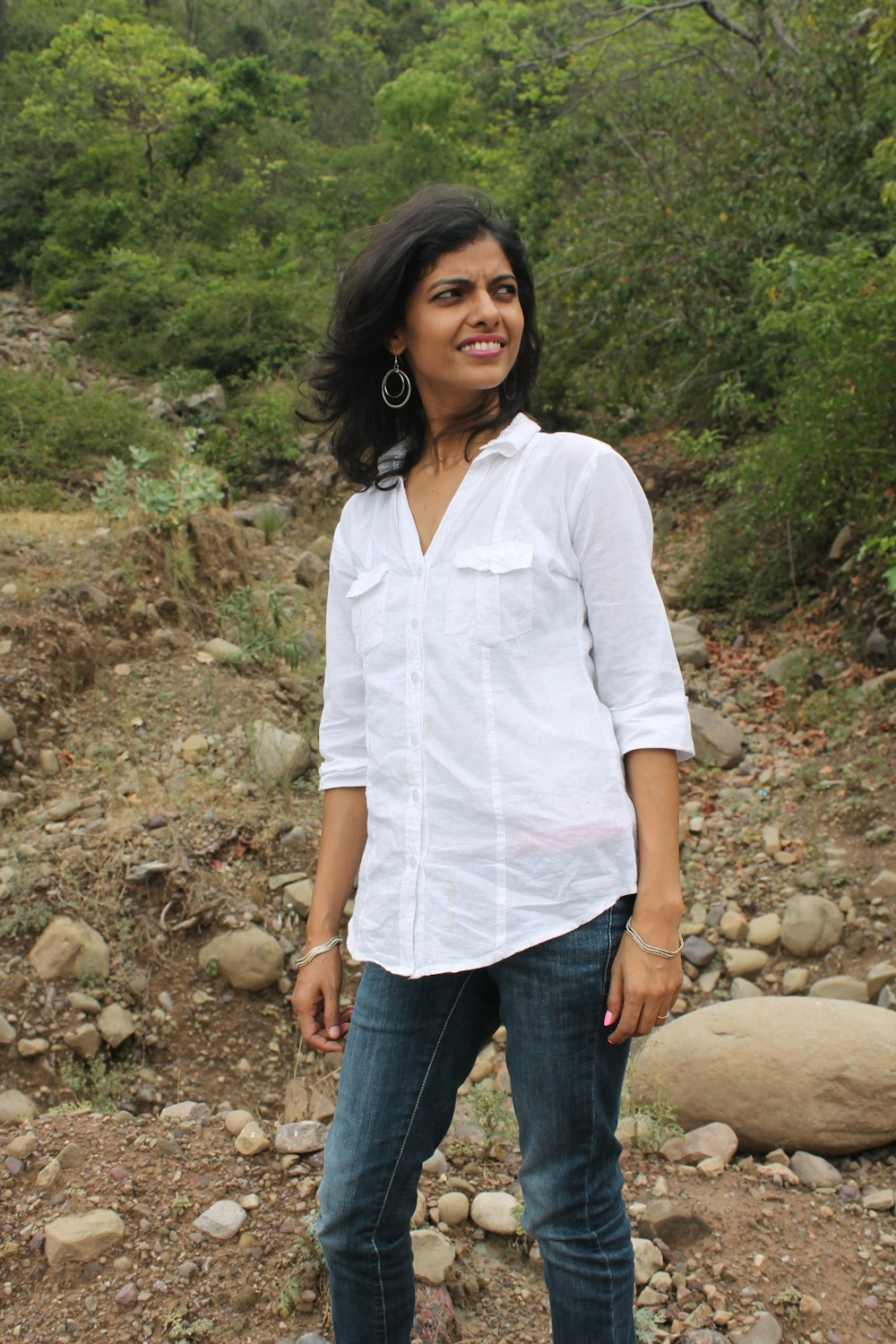 woman in white button up shirt and blue denim jeans standing on rocky ground during daytime